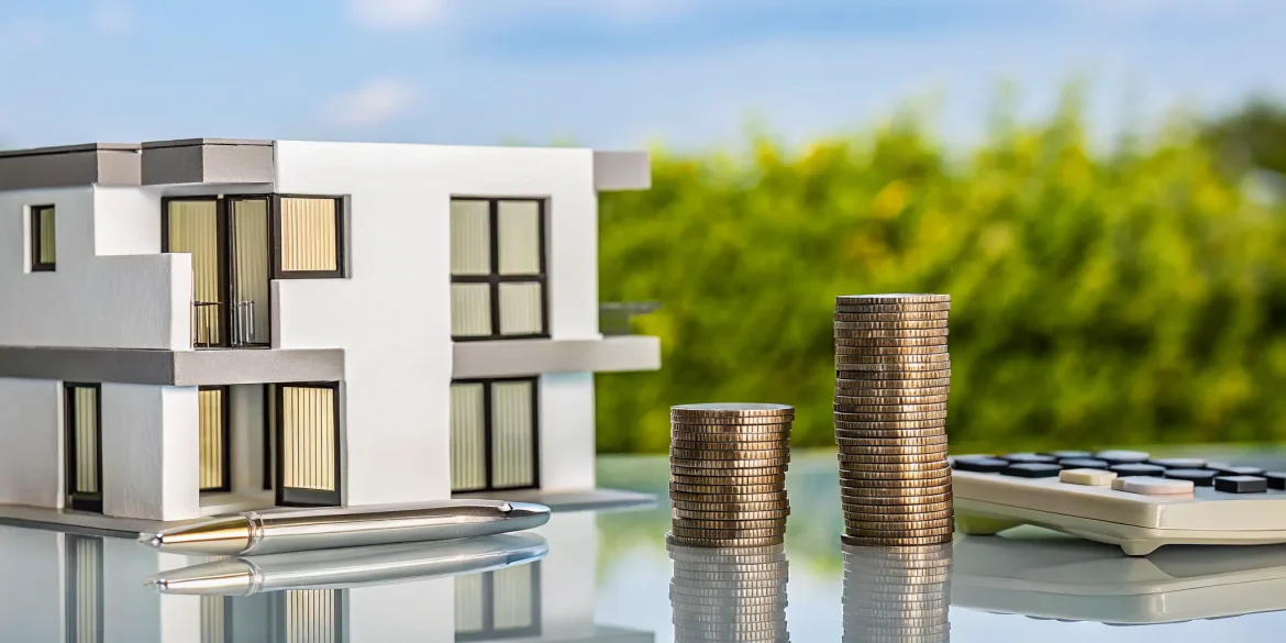Using a calculator to find a low interest rate for an investment property loan with a model house and coins.